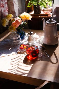 A cup of tea and bouquet of yellow roses and raspberry on white tableat a window in vintage country kitchen, summer morning concept, selective focus, bright light with shadows.