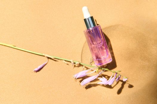Top view. Light violet vial with a cosmetic skin care product and lily of the valley flowers on golden sand background. Minimalistic Beauty art still life. Copy ad space for promotional text