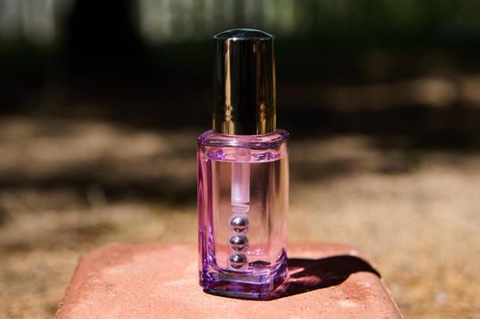 Transparent glass purple bottle with anti-aging cosmetic product for skin care under the eyes on a pink stone, on the nature background. Minimalistic still life. Copy ad space