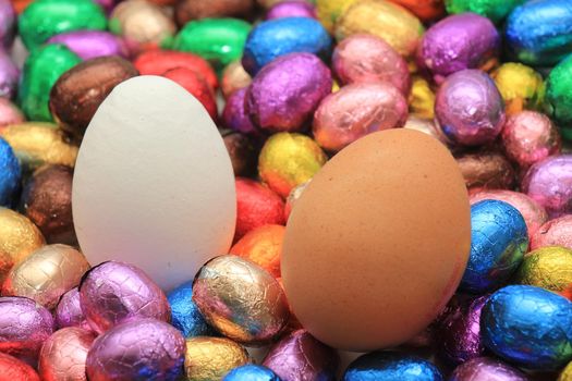 Hen eggs on a pile of colorful wrapped chocolate easter eggs