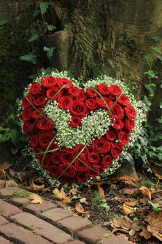 Heart shaped sympathy flowers  or funeral flowers near a tree, red roses