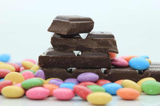 Chocolate filled candies in various bright colors and pieces of a chocolate bar