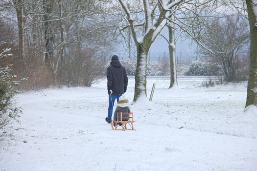 Father and son walking in the snow with a small sleigh