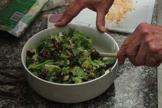 Man preparing a green salad with walnuts, goat cheese and oil