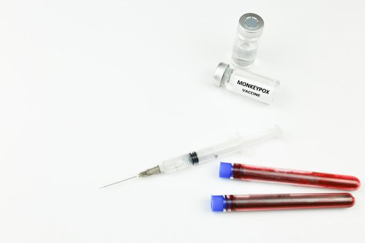 Syringe and vials filled with Monkeypox vaccine next to test tubes with blood on white background