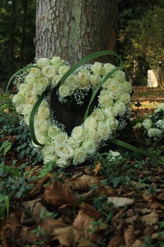 Heart shaped sympathy flowers made from white roses near a tree at a cemetery