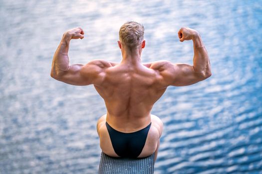 male bodybuilder by the water in nature.