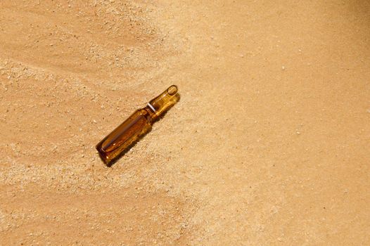 Flat lay of a liquid skin care, anti-aging product, packaging in a dark glass vial on golden sand background with sunlight . Hyaluronic or polyglutamic acid oil cosmetic mockup.