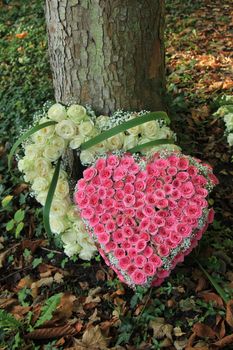 Heart shaped sympathy flowers made from white and pink roses near a tree at a cemetery