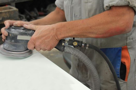 Man in vehicle repair shop, sanding a car part with a grinding machine