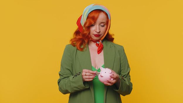 Poor woman upset over insufficient amount of money, holding piggybank and one dollar banknote. Financial crisis. Bankruptcy. Poverty and destitution. Young girl isolated on yellow studio background