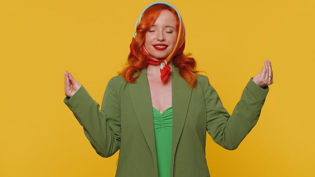 Keep calm down, relax, inner balance. Woman breathes deeply with mudra gesture, eyes closed meditating with concentrated thoughts peaceful mind. Redhead adult girl isolated on yellow studio background