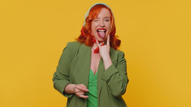 Rock n roll. Overjoyed delighted redhead woman in jacket showing gesture by hands, cool sign, shouting yeah with crazy expression, dancing, emotionally rejoicing in success win alone on yellow wall