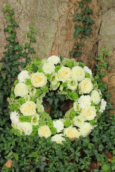 white sympathy wreath or funeral flowers near a tree, white roses and mums