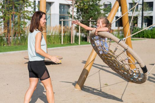 Mom and daughter swing on a round swing. Caucasian woman and little girl have fun on the playground