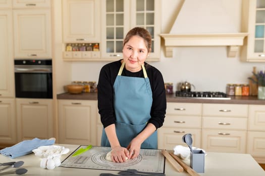 Young smiling Middle Asian woman cooking from dough in modern kitchen, look at camera.