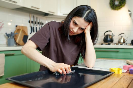 Upset woman cleaning a baking sheet in the kitchen, tired of household chores.