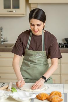 A young housewife in a green apron prepares homemade cakes in a bright kitchen.