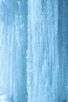 Vertical background of icicles on frozen waterfall wall.