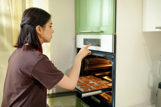 Young brunette woman chooses a program for home baking in a modern built-in oven.