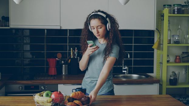 curly caucasian pretty girl with headphones taking photo of breakfast in kitchen at home