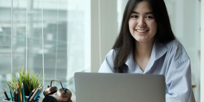 Female student taking notes from a book and using smart phone at home.