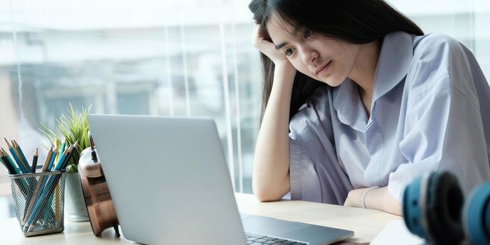 Asian girls are sitting stressed studying online with a tutor on a laptop while sitting in the bedroom at home night. Concept online learning at home.