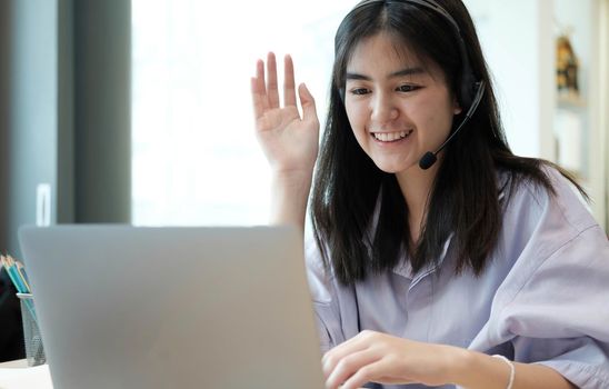 Smiling Asian young female using headset looking at laptop screen listen and learning online courses. Happy chinese business woman with headphones video call for customer service.