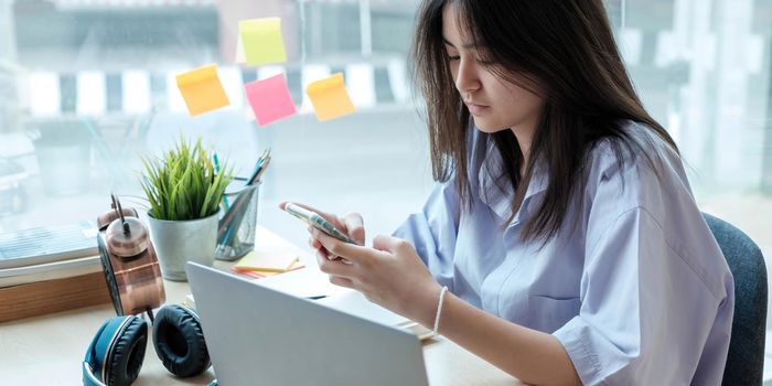 Female student taking notes from a book and using smart phone at home.