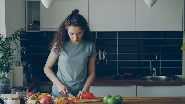 Curly beautiful caucasian woman in headphones dancing prepearing breakfast in kitchen at home