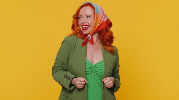 Happy redhead woman in jacket and dress shouting, raising fists in gesture I did it, celebrating success, winning, birthday, lottery goal achievemen. Young girl indoor on yellow studio wall background