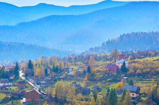 Autumn is one of the four temperate seasons. Outside the tropics, autumn marks the transition from summer to winter. Aerial view of an autumn small village in a valley and mountains in a blue haze