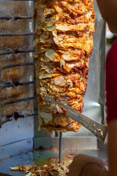 Chef cutting with doner knife Traditional Turkish Doner Kebab meat. Shawarma or gyros. Turkish, greek or middle eastern arab style chicken doner kebab food.