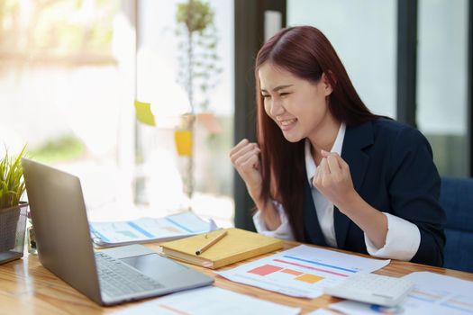 Portrait of a cheerful Asian businesswoman celebrating her victory online with her laptop.