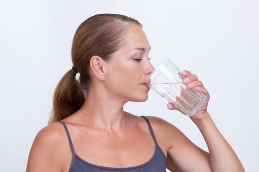 Caucasian middle aged woman holding glass of pure water and drinking on white background