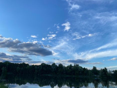 Beautiful sunset on the lake. Clouds and the silhouette of trees are reflected in the water.