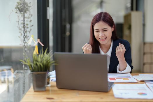 Portrait of a cheerful Asian businesswoman celebrating her victory online with her laptop.