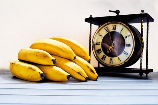 the sweet and fleshy product of a tree or other plant that contains seed and can be eaten as food.Time for a snack with fresh fruits. Yellow ripe bananas and an old clock.