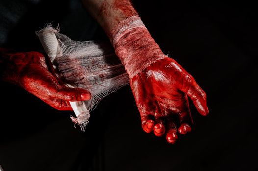 A man covered in blood bandages his hands