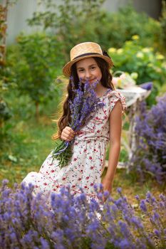 Beautiful long hair girl near lavender bushes at the garden. The girl is walking in the yard and collect flowers. A girl in a hat and dress.