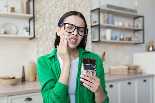 Young beautiful woman eating chocolate bar, having severe toothache at home