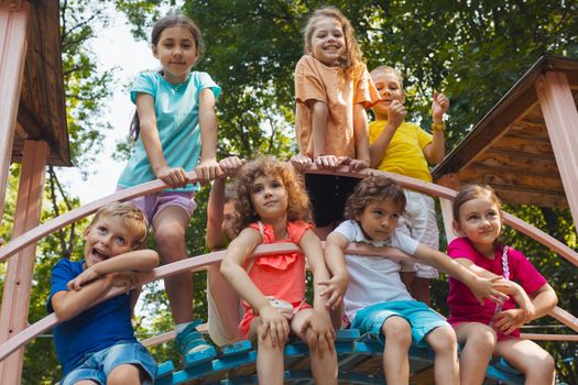 Happy boys and girls stand in the playground in the park. The little children dressed in colorful clothes are showing thumbs up