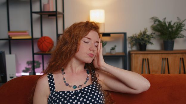 Displeased redhead woman rubbing temples to cure headache problem, suffering from tension and migraine, stress, grimacing in pain, high blood pressure at home. Ginger girl indoors in room on couch