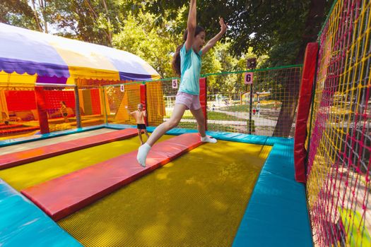 The young children are jumping in the bright trampoline park outdoors in the summer park