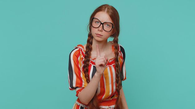 Displeased girl shakes finger and saying no, be careful, scolding and giving advice to avoid danger mistake disapproval disagree warning sign. Redhead teenager child isolated on blue studio background
