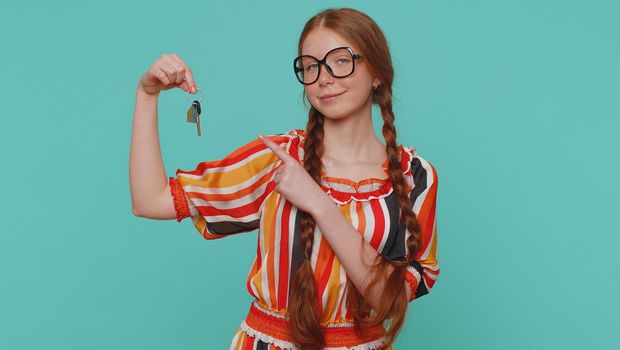 Redhead young girl real estate agent lifting hand showing the keys of new home house apartment, buying or renting property, mortgage loan. Red hair one ginger teenager child on blue studio background