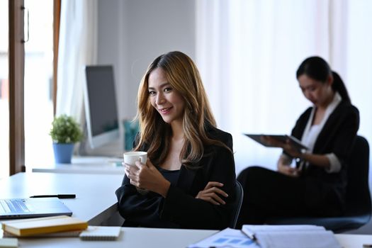 Charming businesswoman holding coffee cup and smiling to camera.