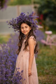 Beautiful long hair girl near lavender bushes at the garden. The girl made a wreath from the flowers