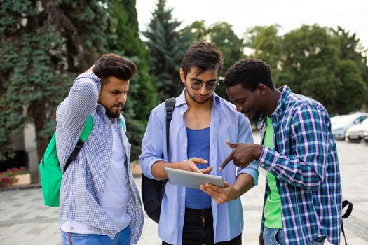 The group of multiethnic students is looking at tablet while is standing outdoors. The african student need to help with navigation