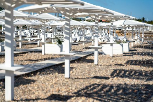 Rows of wooden umbrellas from the sun on the seashore in the morning. Wooden paths on the sand between umbrellas. Beach holiday at the resort